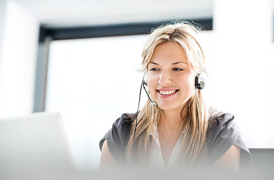 Mid adult smiling female customer service agent with headset is using computer.